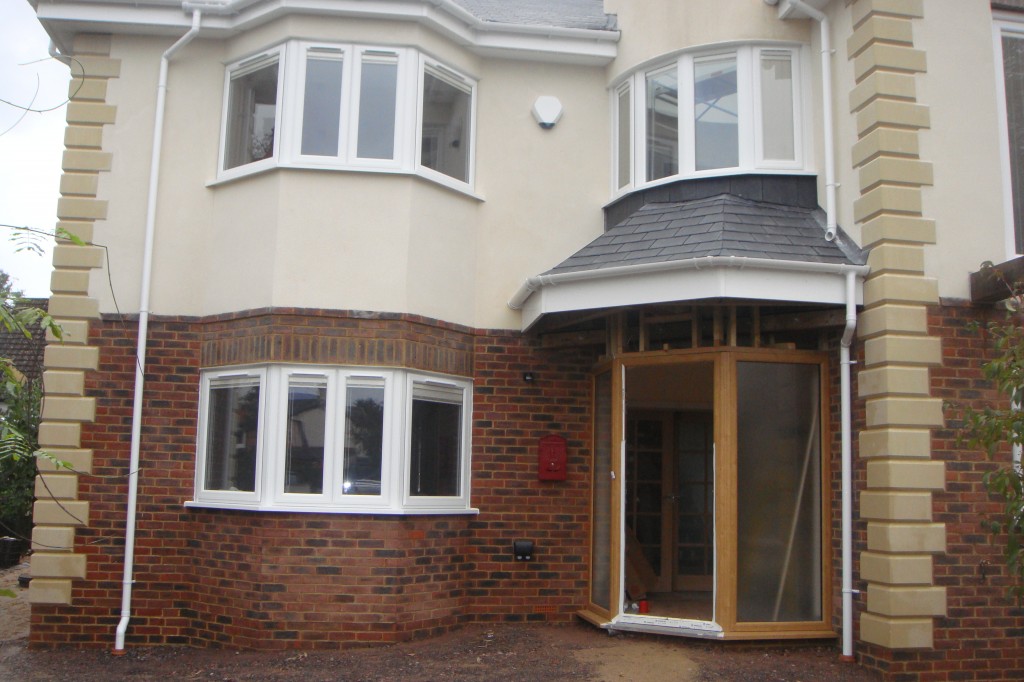 Red brick house with bay windows, rendered upper floor and stone quoins